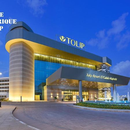 Tolip Resort El Galala Majestic Ain Sukhna Buitenkant foto The photo shows a modern hotel building named "Tolip Resort & Spa," featuring a sleek architectural design with large glass windows. The hotel is illuminated against a twilight sky, showcasing its prominent signage. In the foreground, there is a well
