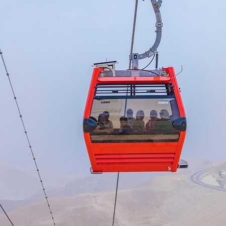 Tolip Resort El Galala Majestic Ain Sukhna Buitenkant foto The photo shows a red gondola lift suspended in the air, traveling along cables. Inside the gondola, a group of people can be seen. The background features a hazy landscape, possibly mountains or hills, indicating an elevated area. The scene conveys 