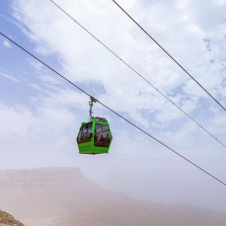 Tolip Resort El Galala Majestic Ain Sukhna Buitenkant foto The photo shows a green cable car suspended in the air, traveling along overhead cables. The backdrop features a hazy landscape, likely mountainous or elevated terrain, with a cloudy sky. The scene suggests a scenic transportation method, possibly us