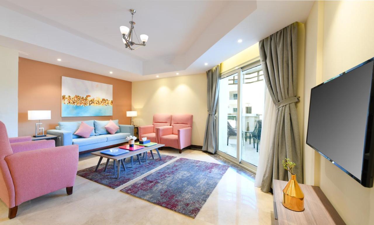 Tolip Resort El Galala Majestic Ain Sukhna Kamer foto The photo shows a modern living room that features a cozy and stylish design. There is a light blue sofa adorned with pastel pink cushions, accompanied by two pink armchairs. A coffee table sits in front, placed on a colorful area rug that adds warmt