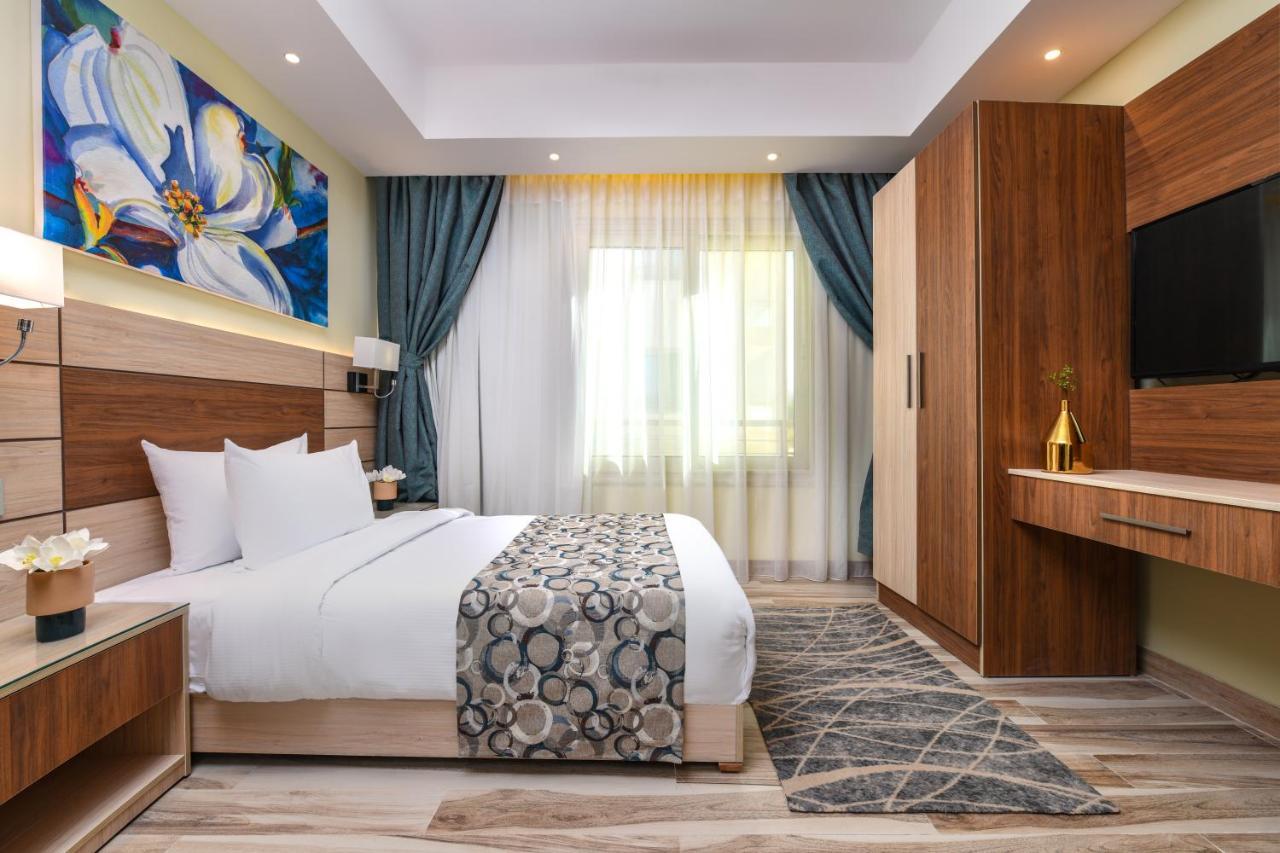 Tolip Resort El Galala Majestic Ain Sukhna Buitenkant foto The photo shows a well-designed hotel room. It features a comfortable bed with a decorative bedspread and two pillows. There are soft curtains framing a window that lets in natural light. On one side, there is a colorful piece of artwork hanging on t