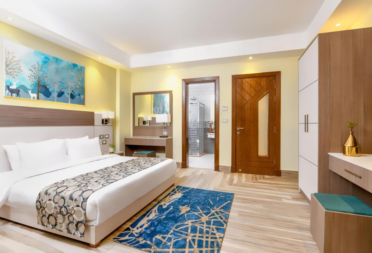 Tolip Resort El Galala Majestic Ain Sukhna Buitenkant foto The photo shows a well-decorated hotel room. There is a large bed with white linens and a decorative throw blanket. The room features a wooden wardrobe and a bedside table with lamps. A colorful rug is placed on the floor, adding warmth to the space.