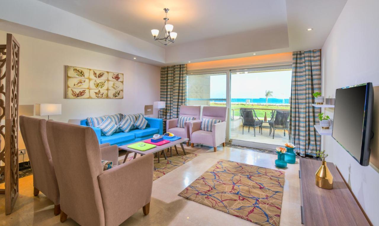 Tolip Resort El Galala Majestic Ain Sukhna Buitenkant foto The photo shows a bright and modern living room. It features a blue sofa with decorative cushions, two light-colored armchairs, and a coffee table. A large area rug adds warmth to the space, which is decorated with a subtle pattern. The walls have so