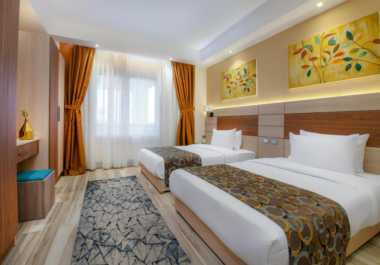 Tolip Resort El Galala Majestic Ain Sukhna Buitenkant foto The photo shows a modern hotel room with two single beds, each covered with white linens and decorative brown bed throws. The walls are painted in warm colors, and there are two pieces of artwork featuring floral and leaf designs above the beds. The 