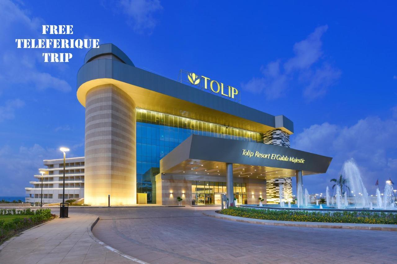 Tolip Resort El Galala Majestic Ain Sukhna Buitenkant foto The photo shows a modern hotel building named "Tolip Resort & Spa," featuring a sleek architectural design with large glass windows. The hotel is illuminated against a twilight sky, showcasing its prominent signage. In the foreground, there is a well