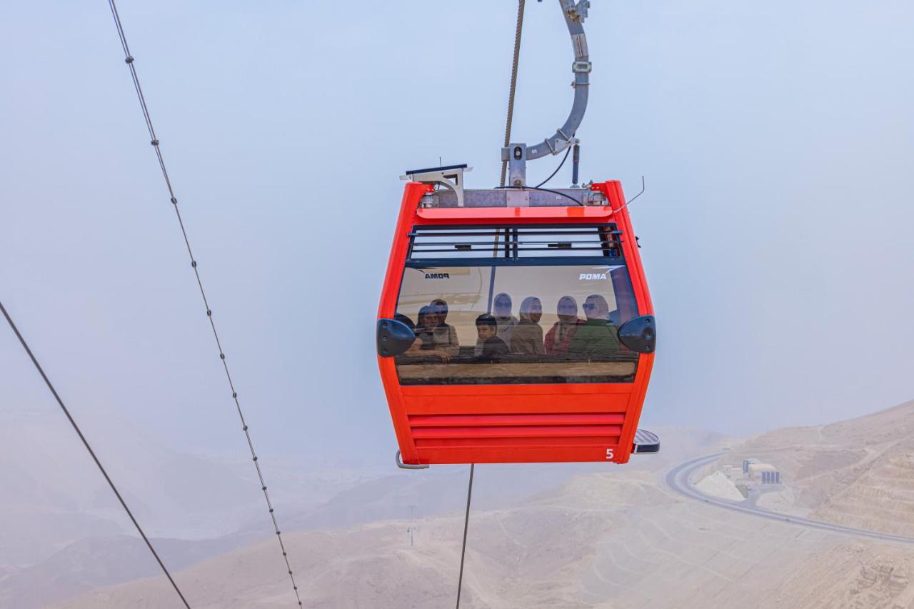 Tolip Resort El Galala Majestic Ain Sukhna Buitenkant foto The photo shows a red gondola lift suspended in the air, traveling along cables. Inside the gondola, a group of people can be seen. The background features a hazy landscape, possibly mountains or hills, indicating an elevated area. The scene conveys 