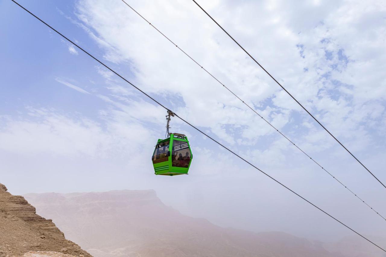 Tolip Resort El Galala Majestic Ain Sukhna Buitenkant foto The photo shows a green cable car suspended in the air, traveling along overhead cables. The backdrop features a hazy landscape, likely mountainous or elevated terrain, with a cloudy sky. The scene suggests a scenic transportation method, possibly us