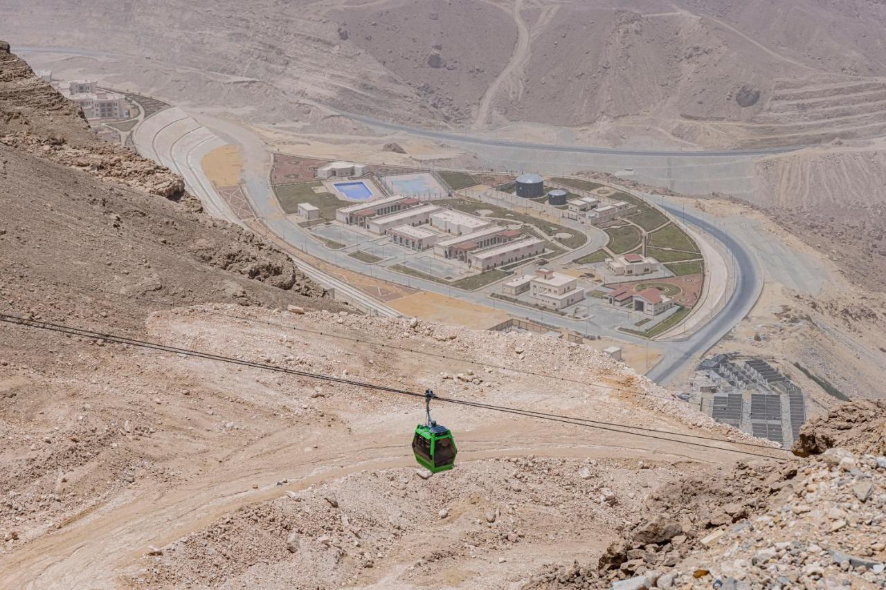 Tolip Resort El Galala Majestic Ain Sukhna Buitenkant foto The photo shows a mountainous landscape with a steep, dry terrain. In the foreground, there is a green cable car or gondola traveling along a cable. Below, a complex of buildings and roads can be seen, likely part of a resort or recreational area. Th