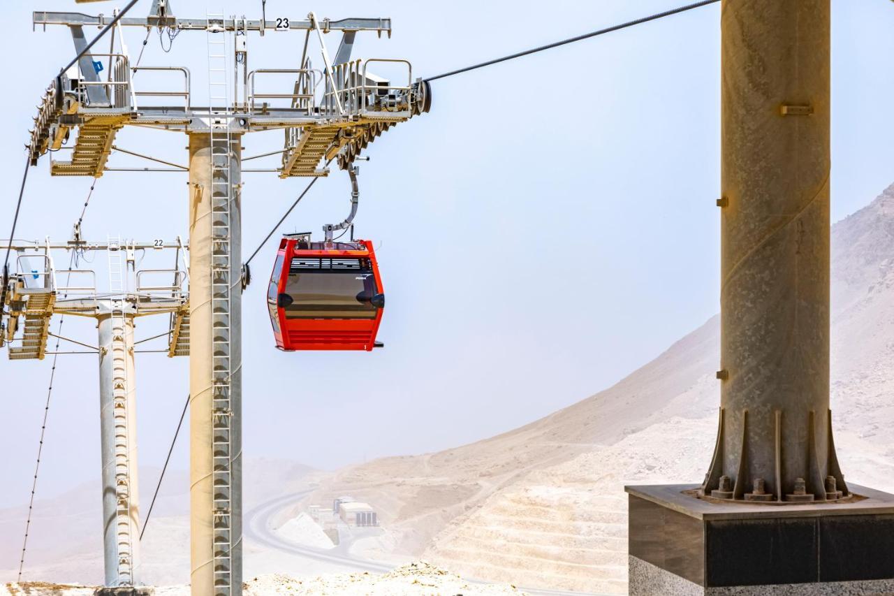 Tolip Resort El Galala Majestic Ain Sukhna Buitenkant foto The photo shows a cable car system with a single red gondola suspended mid-air. It appears to be part of a larger cable car infrastructure, with metal pylons supporting the cables above. The background features a hazy landscape, likely characterized 