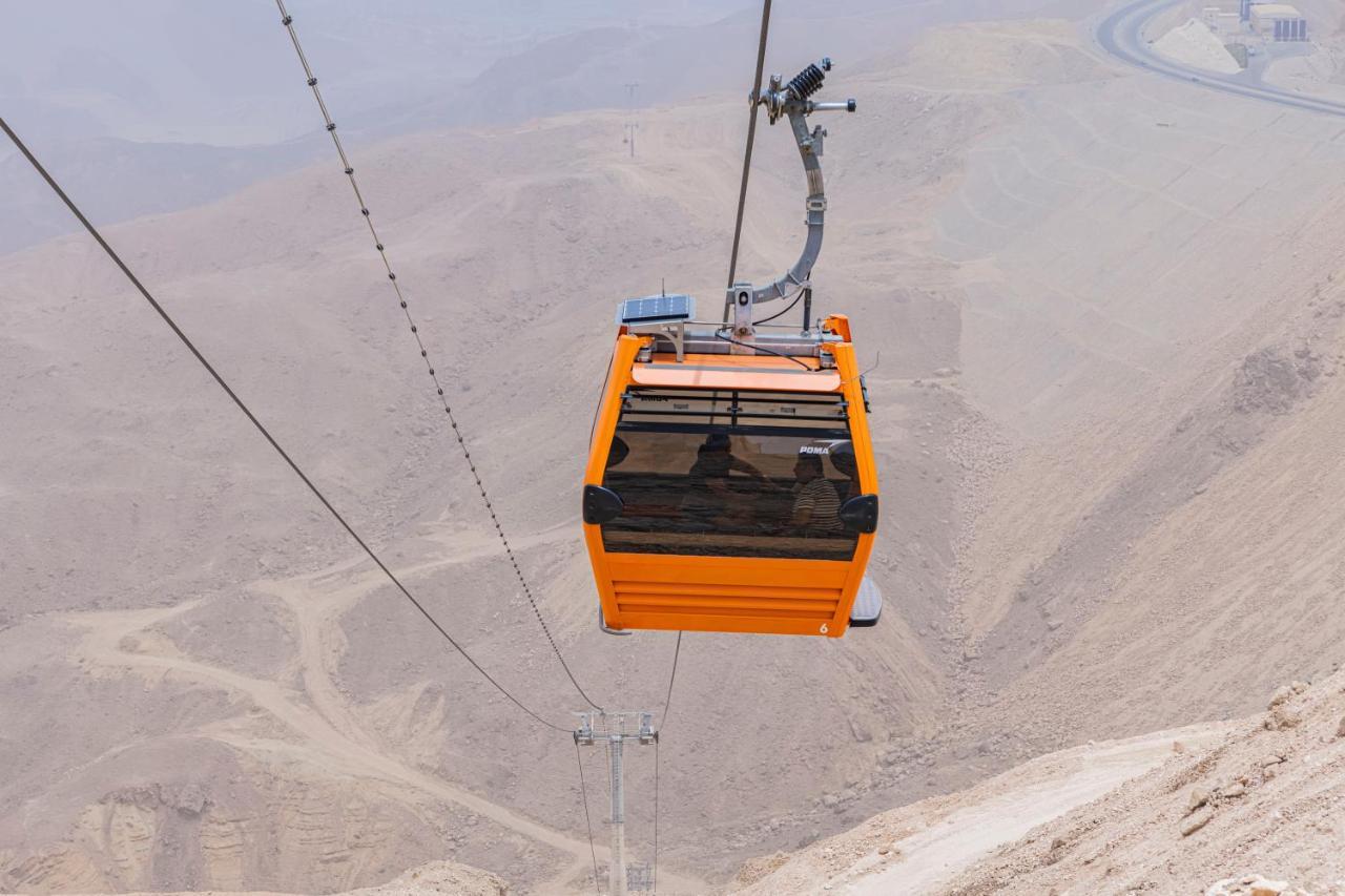 Tolip Resort El Galala Majestic Ain Sukhna Buitenkant foto The photo shows an orange cable car suspended in the air, traveling along a set of cables. It appears to be located in a mountainous or hilly area, with rugged terrain and dry, rocky landscapes visible below. The background features slopes that seem 