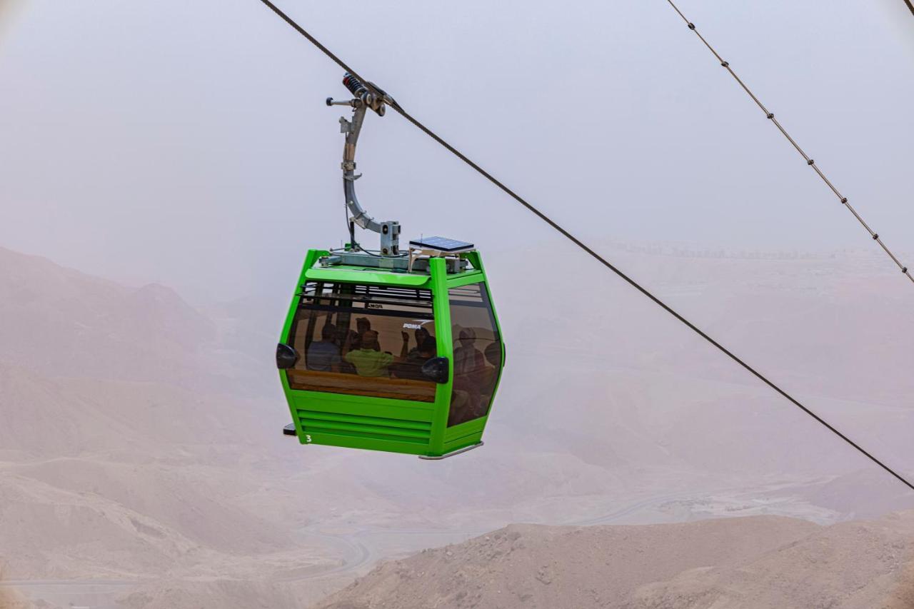 Tolip Resort El Galala Majestic Ain Sukhna Buitenkant foto The photo shows a green cable car suspended in the air, moving along a wire. The cable car appears to be traversing a mountainous landscape, which looks rocky and arid. The surrounding environment is somewhat foggy or hazy, suggesting limited visibil