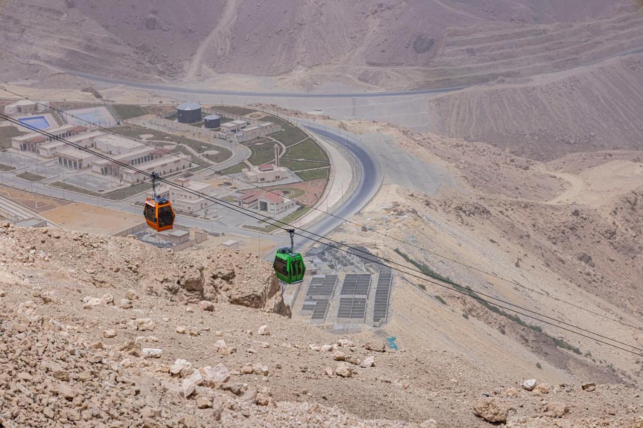Tolip Resort El Galala Majestic Ain Sukhna Buitenkant foto The photo shows a scenic view from a high elevation, featuring a cable car system. Two cable cars are visible, one orange and one green, traveling along cables down the mountainside. Below, there appears to be a developed area with roads and light st