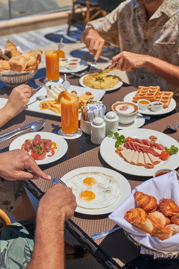 Tolip Resort El Galala Majestic Ain Sukhna Buitenkant foto The photo features a spread of breakfast dishes on a table. There are two sunny-side-up eggs on one plate, surrounded by various food items, including slices of ham, sausages, and fresh tomatoes. Another plate holds a serving of waffles. A bowl with 