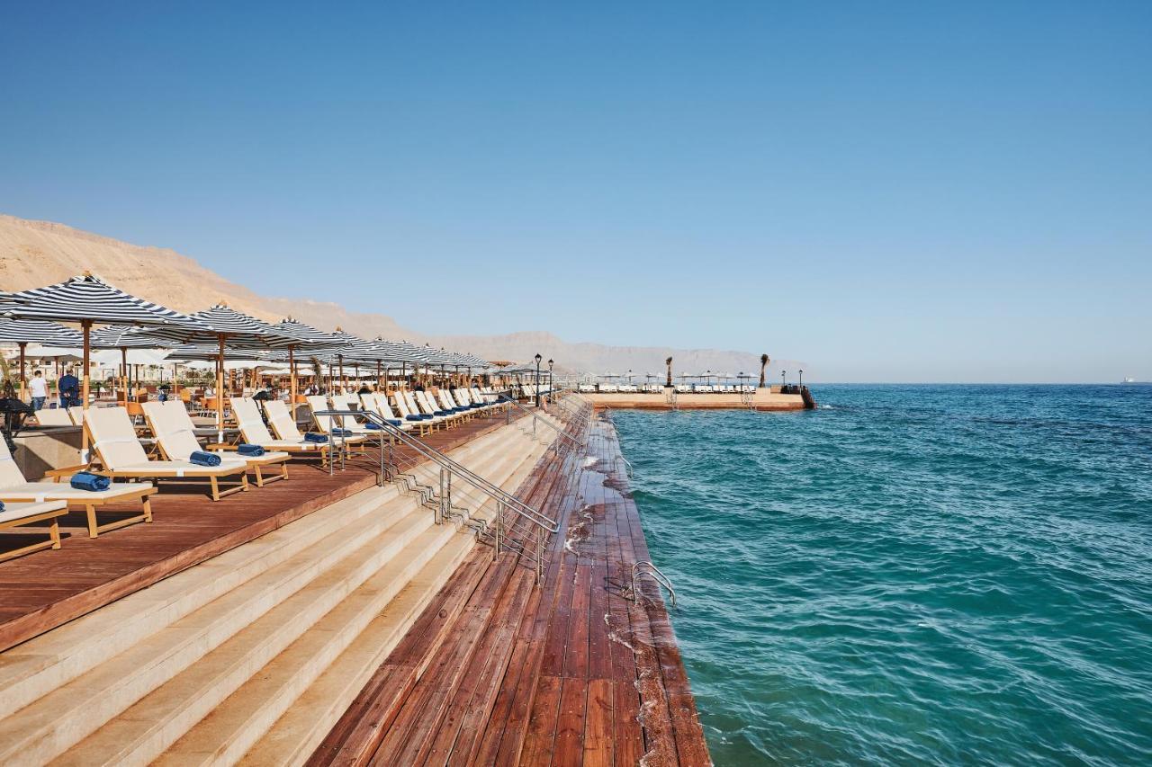 Tolip Resort El Galala Majestic Ain Sukhna Buitenkant foto The photo shows a seaside area featuring a wooden deck that extends into the water. On the left side, there are several lounge chairs arranged neatly under shade structures, suggesting a relaxing atmosphere. The ocean is visible in the foreground, wi