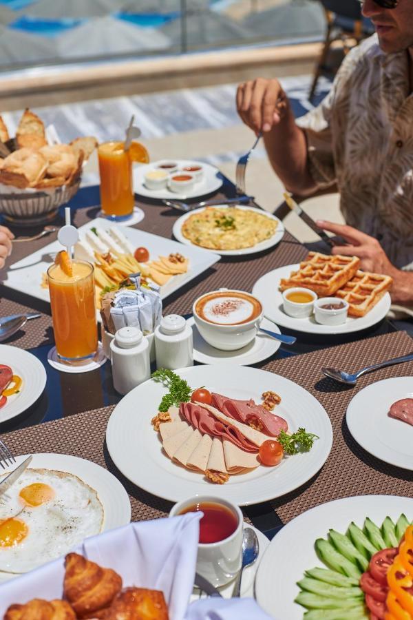 Tolip Resort El Galala Majestic Ain Sukhna Buitenkant foto The photo shows a breakfast spread laid out on a table. There are several plates with a variety of food items, including:

1. **Sliced Cold Cuts**: A plate featuring various cold meats, accompanied by garnishes like cherry tomatoes and lettuce.
2. **