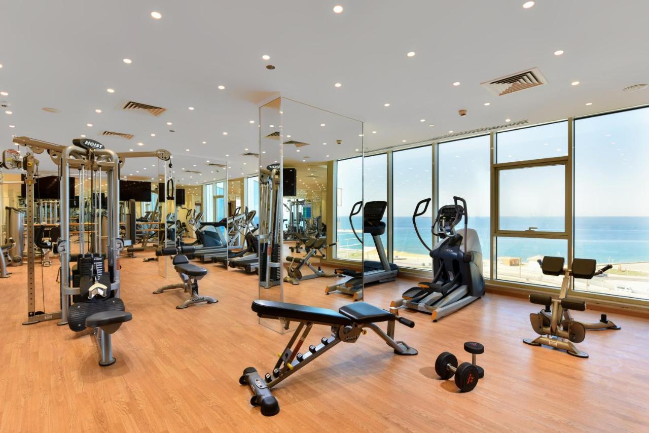 Tolip Resort El Galala Majestic Ain Sukhna Buitenkant foto The photo shows a modern gym interior with a variety of fitness equipment. There are cardio machines like treadmills and ellipticals, along with strength training equipment such as free weights and benches. The gym features large windows that offer a