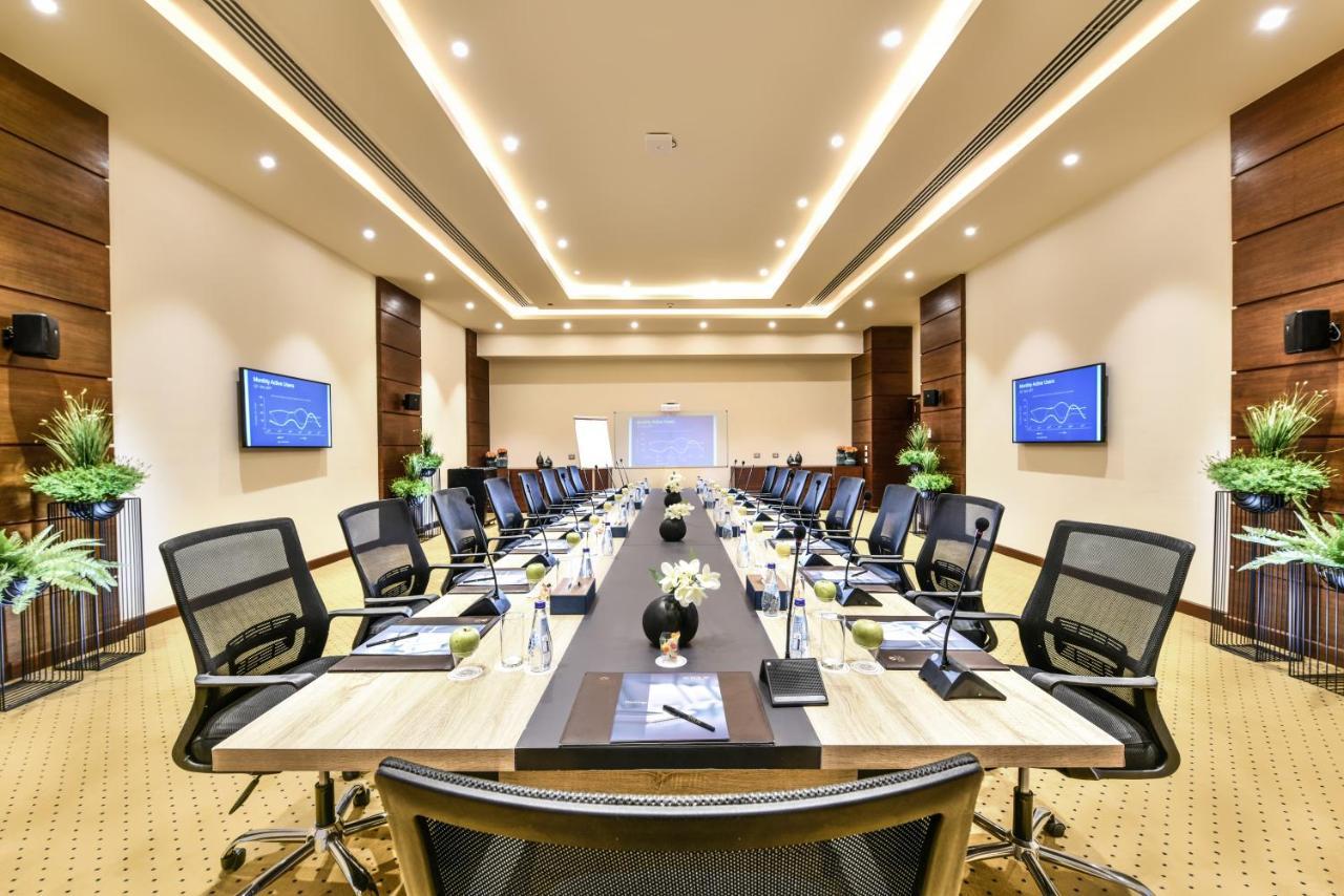 Tolip Resort El Galala Majestic Ain Sukhna Buitenkant foto The photo shows a modern conference room designed for meetings. It features a long rectangular table at the center, surrounded by ergonomic black chairs. The room is well-lit with ceiling lights and has a neutral color scheme. There are two large scr