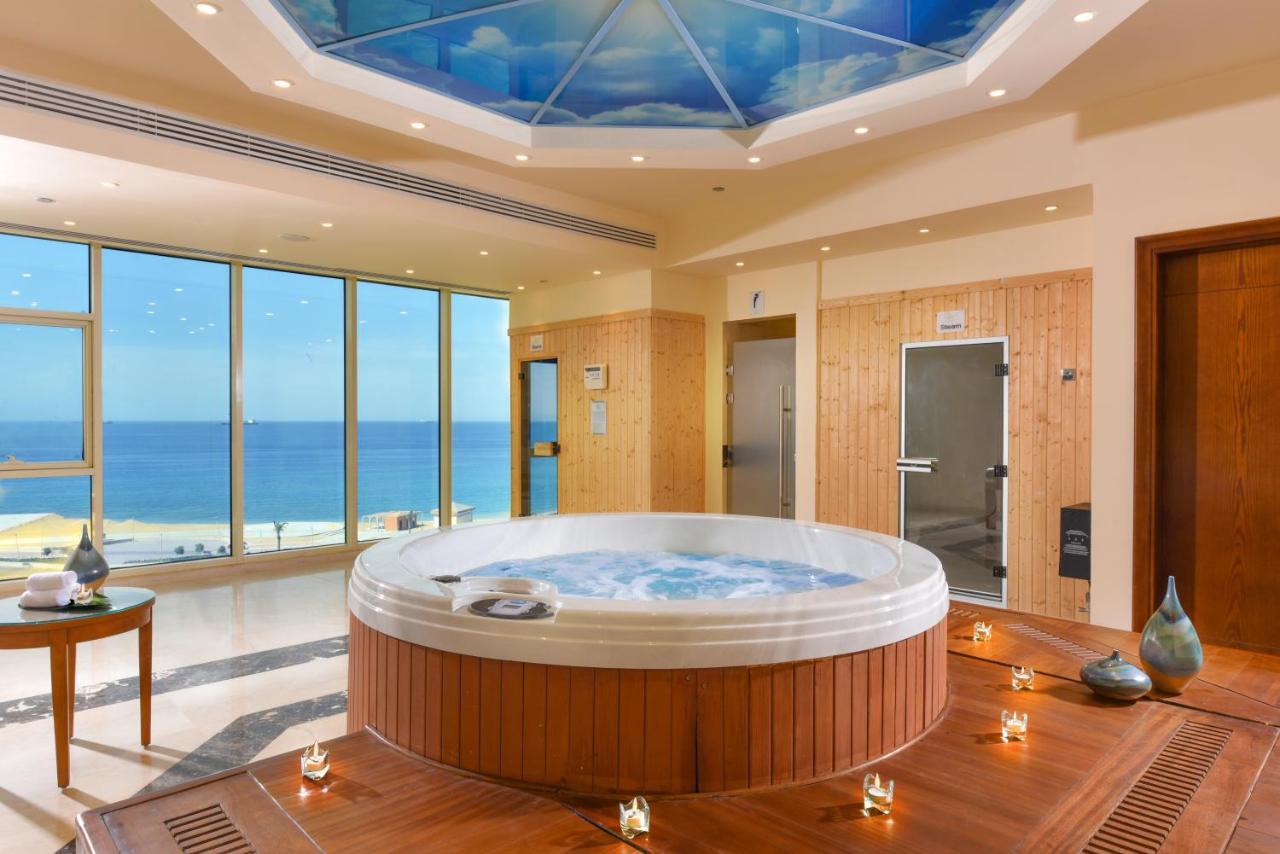 Tolip Resort El Galala Majestic Ain Sukhna Buitenkant foto The photo shows a luxurious spa room featuring a large, round hot tub positioned in the center. The walls are mostly glass, offering a stunning view of the ocean. The ceiling has a painted sky, enhancing the serene atmosphere. There are wooden elemen