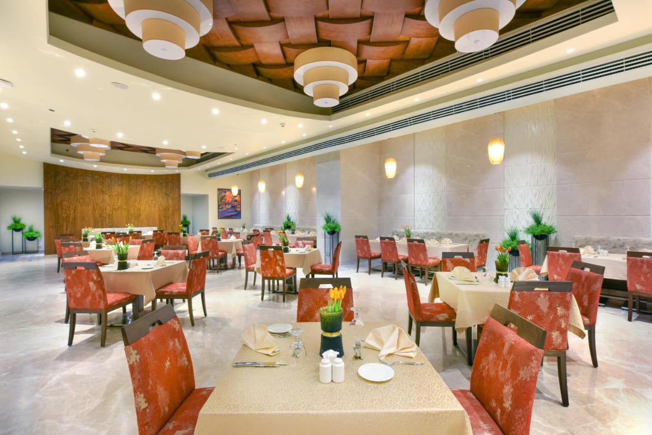 Tolip Resort El Galala Majestic Ain Sukhna Buitenkant foto The photo shows the interior of a restaurant. The space features several tables set with light-colored tablecloths and chairs with reddish upholstery. Each table is adorned with decorative napkins and has small plants in the center. The room has a mo