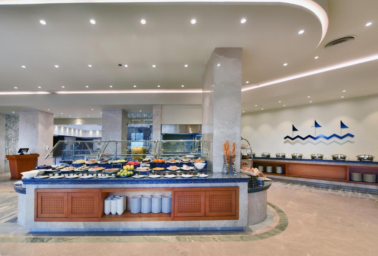Tolip Resort El Galala Majestic Ain Sukhna Buitenkant foto The image shows a buffet-style dining area in a restaurant or hotel. There are several food stations with a variety of dishes displayed, including fruits, salads, and other food items. The layout features a large, central island with a wooden base an