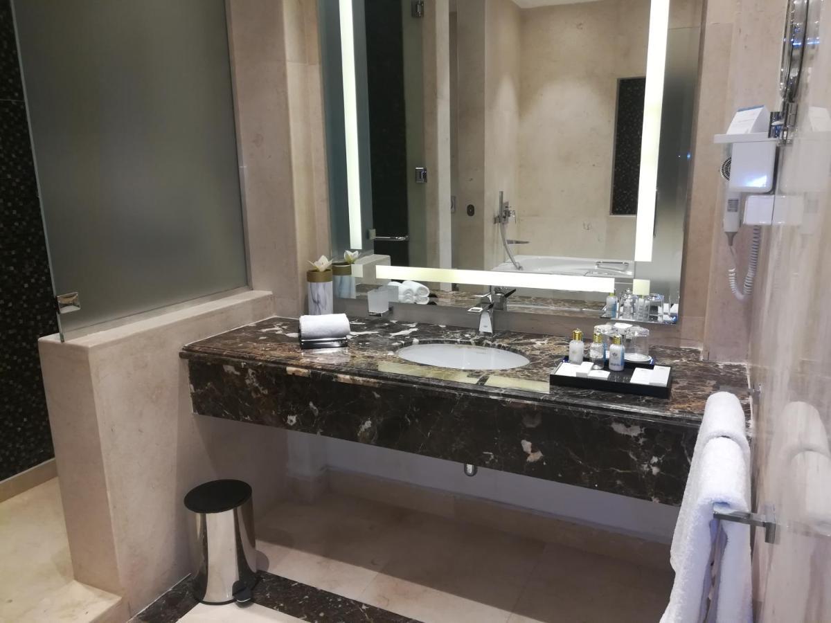 Tolip Resort El Galala Majestic Ain Sukhna Buitenkant foto The photo shows a modern bathroom with elegant design features. There is a large vanity made of dark marble with a sink and a set of toiletries neatly arranged on top. A mirror with built-in lighting is mounted above the sink. To the side, there is a