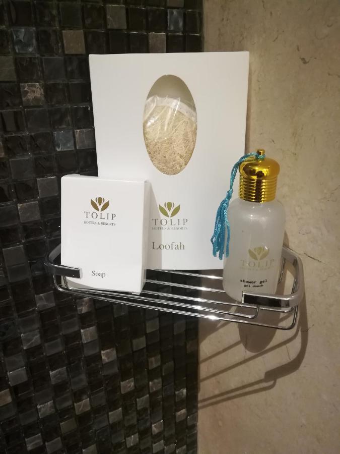 Tolip Resort El Galala Majestic Ain Sukhna Buitenkant foto The photo shows a small metal shelf containing three items related to personal care. 

1. **Soap**: A white box labeled "TOLIP" with the word "Soap" visible on the front.
2. **Loofah**: A package with the same "TOLIP" branding, containing loofah.
3. 