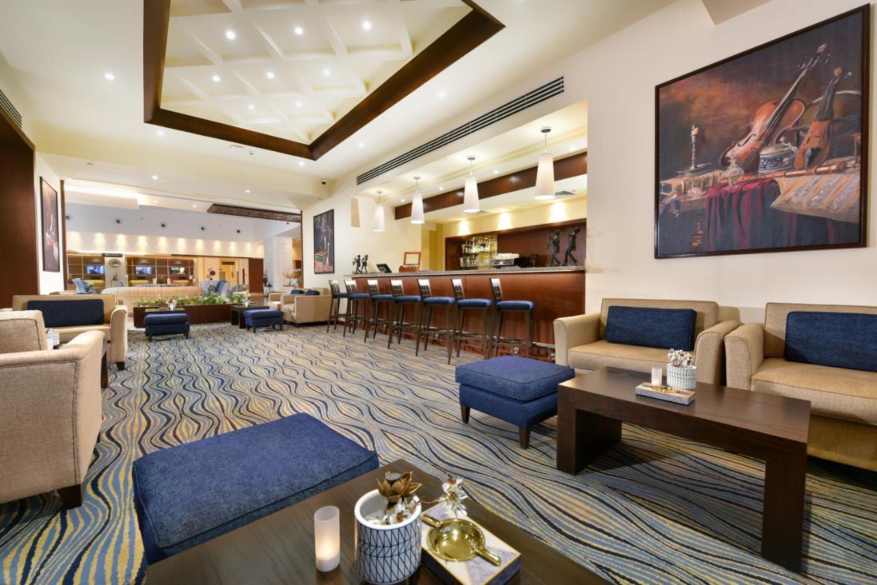 Tolip Resort El Galala Majestic Ain Sukhna Buitenkant foto The photo depicts a modern, inviting lobby or lounge area. It features a cozy seating arrangement with light-colored sofas and deep blue accent chairs. In the center, there is a low wooden coffee table with decorative items, including a candle and sm