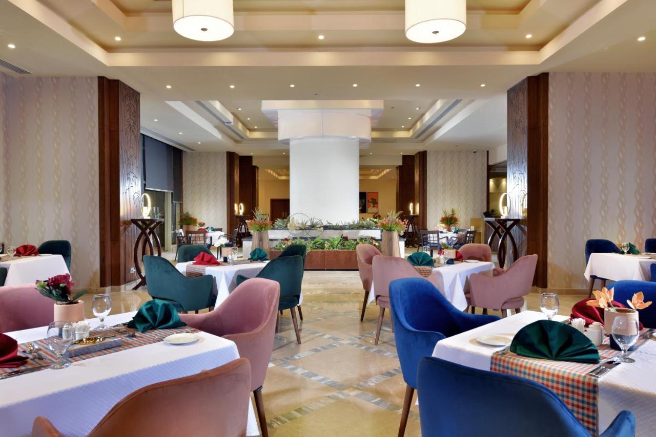 Tolip Resort El Galala Majestic Ain Sukhna Buitenkant foto The photo shows a spacious and elegantly designed restaurant interior. The layout includes several round tables dressed in white tablecloths, each set with decorative plates, cutlery, and colorful napkins. The chairs are upholstered in a variety of c