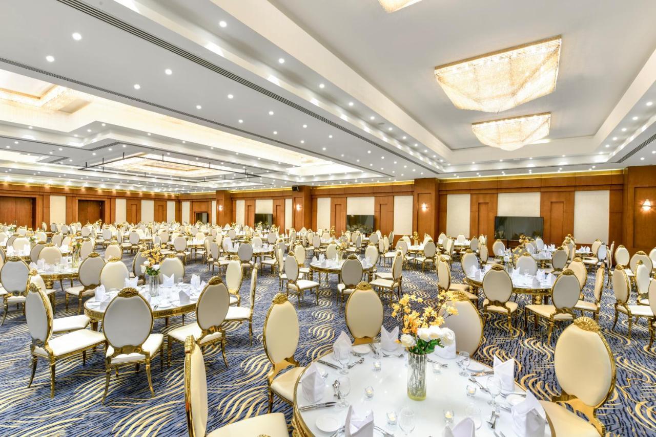 Tolip Resort El Galala Majestic Ain Sukhna Buitenkant foto The photo shows a spacious and elegantly decorated banquet hall. The room features numerous round dining tables, each set with white tablecloths and adorned with decorative centerpieces, likely flowers. The chairs surrounding the tables have a luxuri